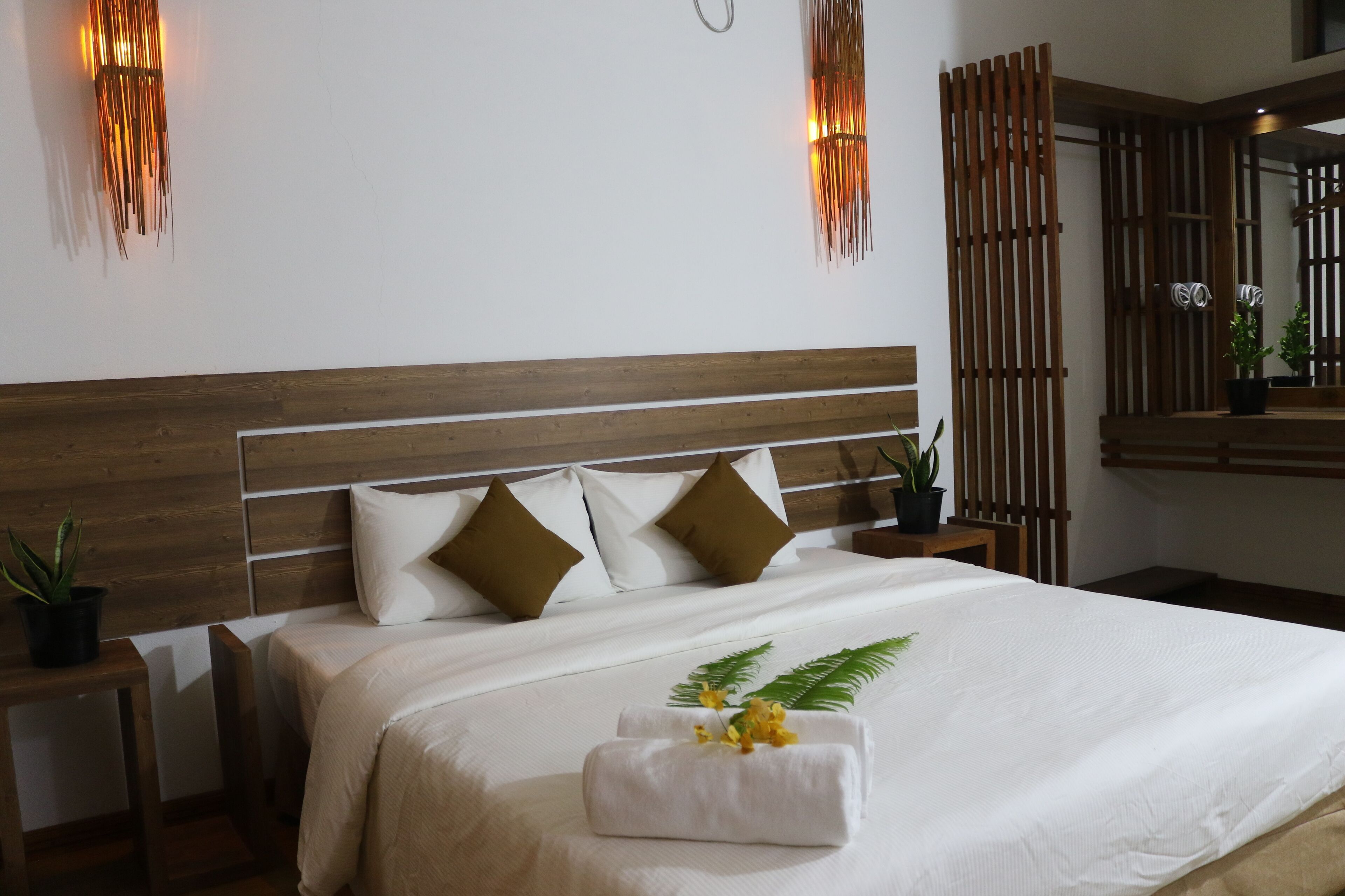A neatly made bed with a wooden headboard, white bedding, and decorative pillows. There are wall-mounted light fixtures and a mirror above the bed.
