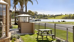 A patio area with a table and bench, a covered seating area, and a view of a body of water and hills in the background. - Riviera Beach Resort (Lakes Entrance)