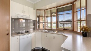 A modern kitchen with white cabinets, a black stove, and a large window offering a view of the outdoors. - Riviera Beach Resort (Lakes Entrance)