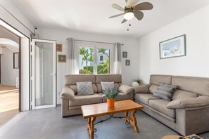 Sala de estar com sofá bege, mesa de centro de madeira e ventilador de teto.