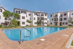 Uma piscina com deck ladrilhado, cercada por edifícios brancos com varandas e janelas em arco.