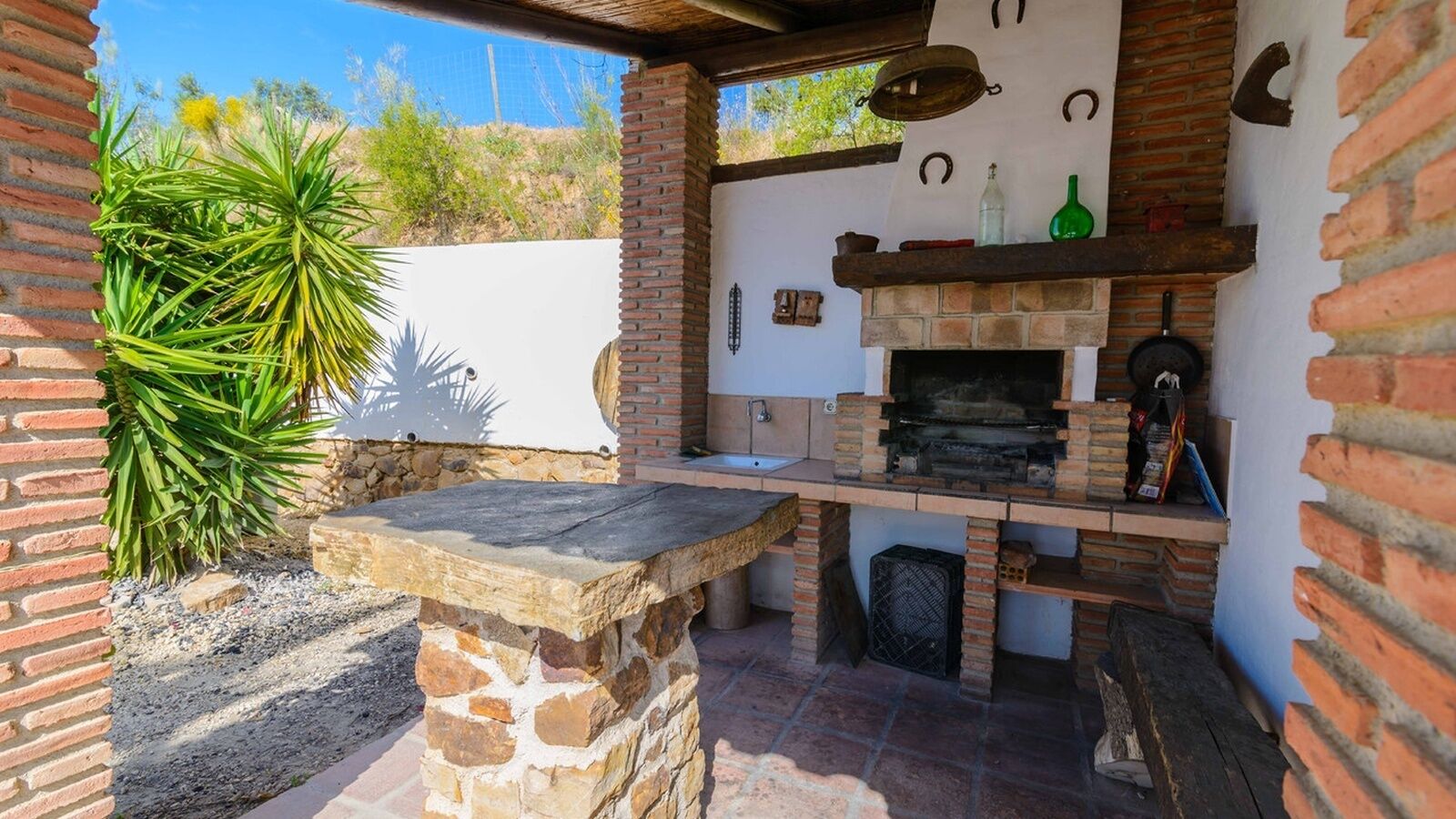 An outdoor kitchen with a stone table, brick oven, and a sink.