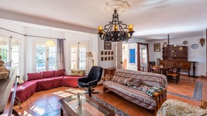 A spacious living room with a red sofa, a patterned sofa, a black armchair, and a glass coffee table. There is a piano and a dining table with chairs in the background. - El Olivo de Macharaviaya by Ruralidays (Málaga)