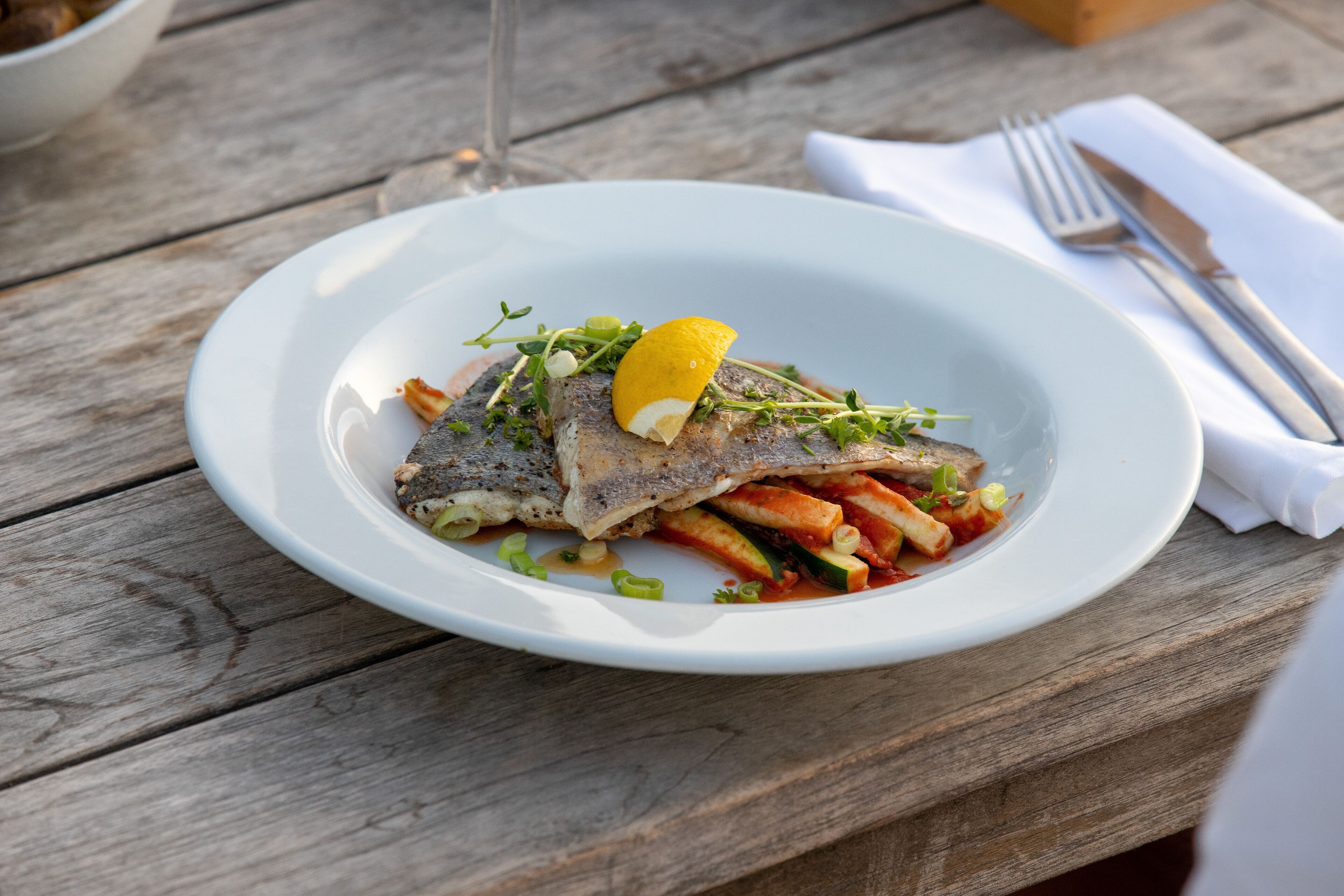 A white plate with fish, vegetables, and a lemon slice on a wooden table.