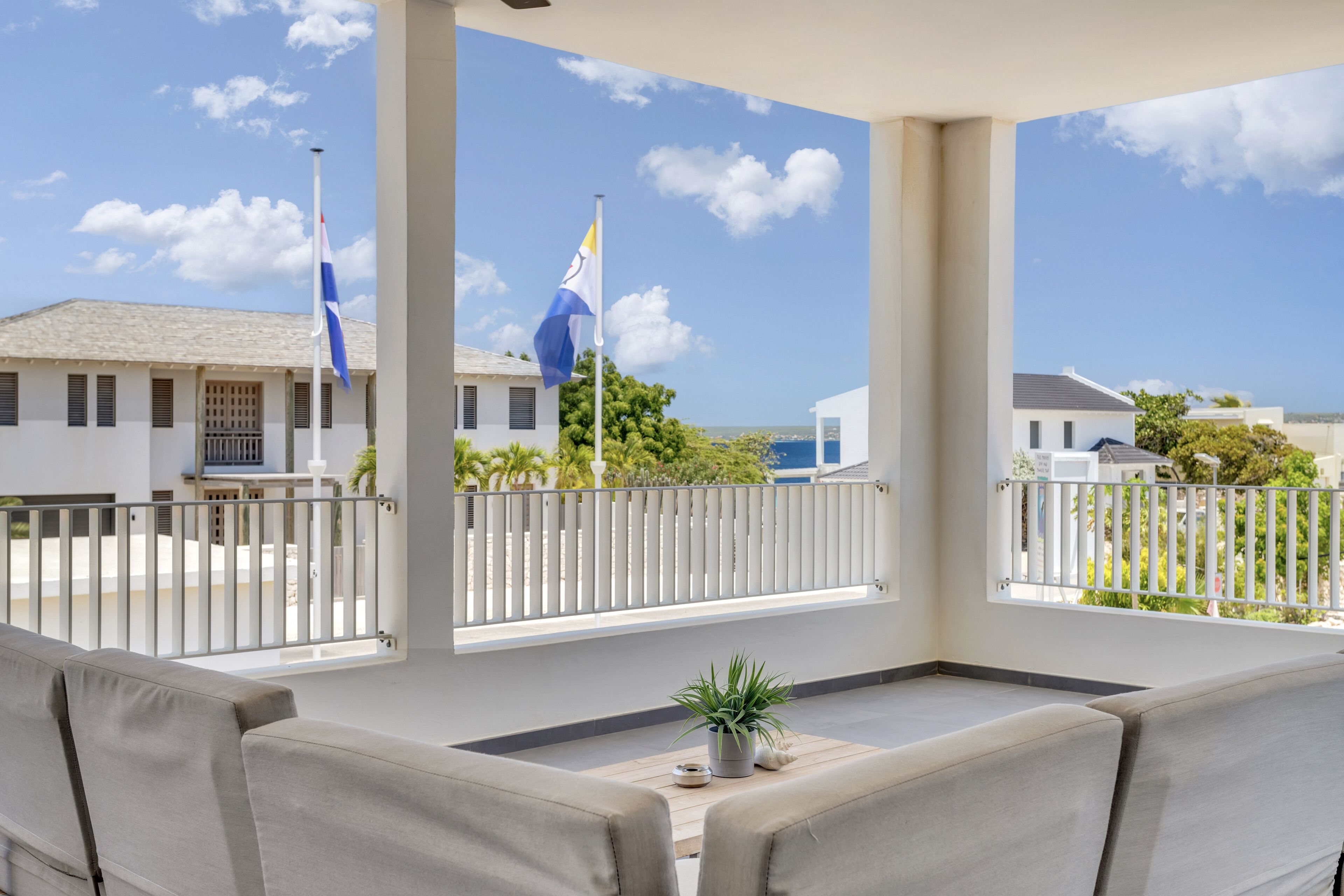 Een balkon met uitzicht op zee, een vlag en een bloempot.