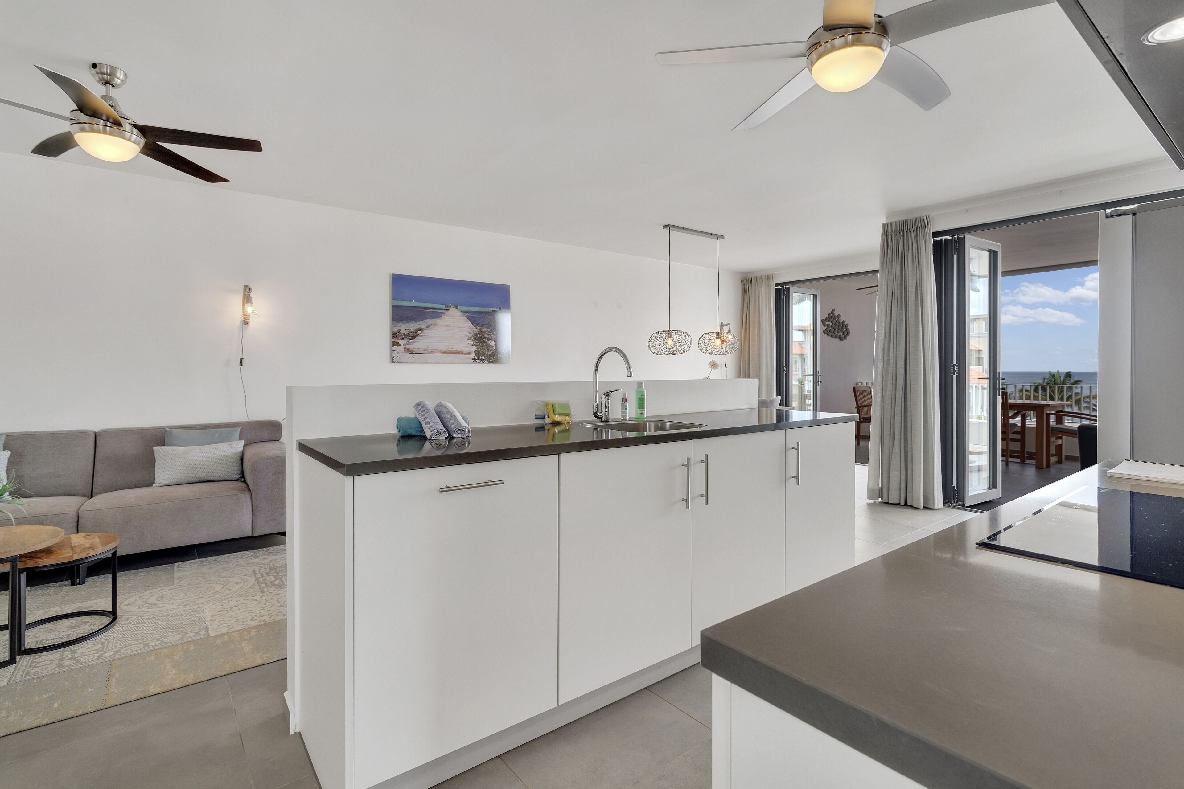 A modern kitchen with white cabinets, a central island, and a dining area with a sofa and coffee table.