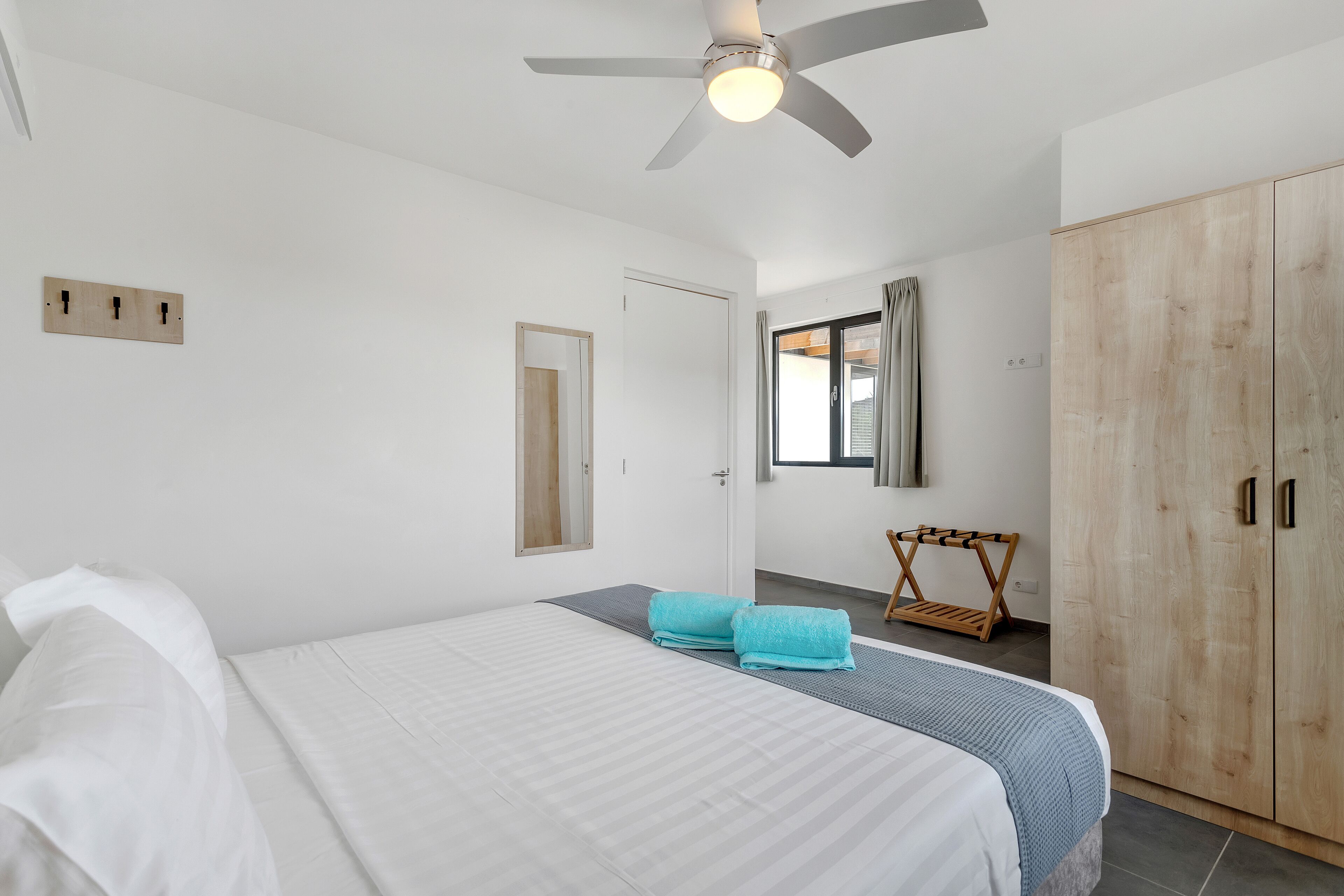 Une chambre à coucher avec un lit, un ventilateur de plafond, une armoire et une fenêtre avec des rideaux.
