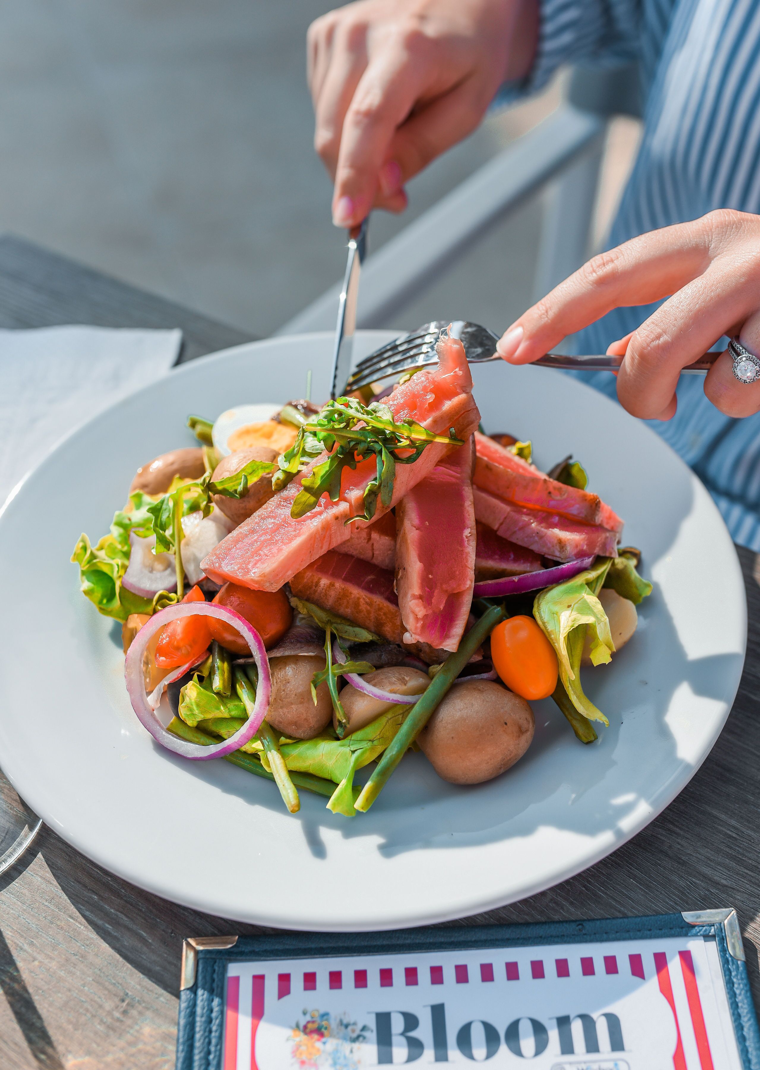 A plate of food with various vegetables and a slice of meat, held by a person with a fork.