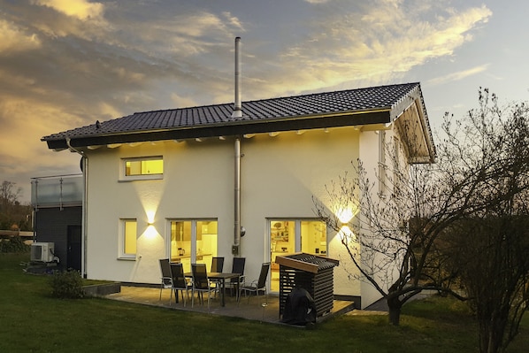 A modern two-story house with a tiled roof, a chimney, and a patio with outdoor seating.