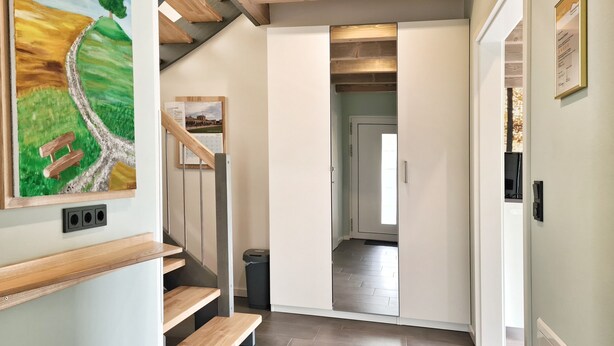 Ein modernes Interieur mit einer Holztreppe, einem Landschaftsbild und Blick in einen anderen Raum.
