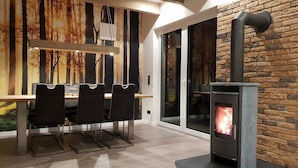 Ein moderner Essbereich mit Holztisch und Stühlen, einem Kamin und einem großen Fenster mit Blick auf Bäume.