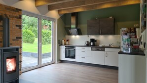 Eine moderne Küche mit Kaminofen, weißen Schränken und Blick auf einen grünen Garten durch große Schiebetüren.