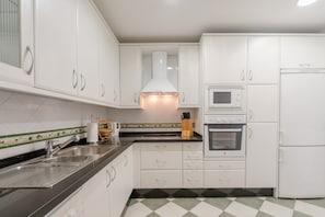 A kitchen with white cabinets, a stainless steel sink, a microwave, an oven, and a refrigerator.