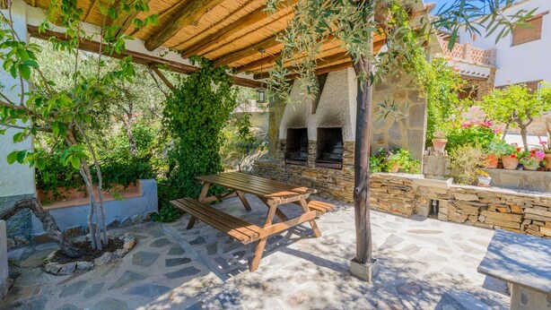 Une terrasse extérieure avec une table et des bancs en bois, un sol en pierre et un mur en pierre.