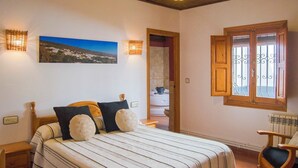 A bedroom with a bed, a chair, a painting, and a window with bars. - Balcón de Válor 3 by Ruralidays (Granada)