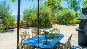 An outdoor patio with a glass table and chairs, surrounded by greenery and a stone structure. - Balcón de Válor 3 by Ruralidays (Granada)