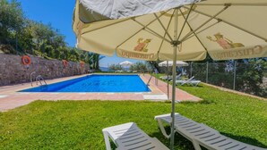 Une piscine équipée d’une bouée de sauvetage, une zone herbeuse et des chaises longues disposées sous un auvent.