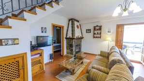 Un salon avec une cheminée en pierre, un canapé, un téléviseur et un escalier.