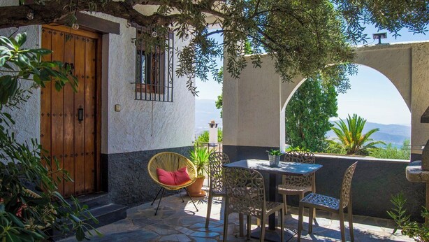 A patio with a table and chairs, a wicker chair, a potted plant, and a view of the sea. - Balcón de Válor 5 by Ruralidays (Granada)