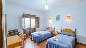 A room with two single beds, a wooden desk, a chair, and a window with wooden shutters. - Balcón de Válor 6 by Ruralidays (Granada)