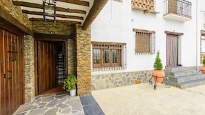 Facciata in pietra con porte in legno, una piccola pianta in vaso e una scala che conduce a un balcone.