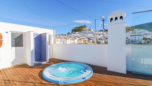 A rooftop deck with a hot tub, a covered seating area, and a view of a white-washed town with a prominent tower. - Ardales 2 pax by Ruralidays (Málaga)