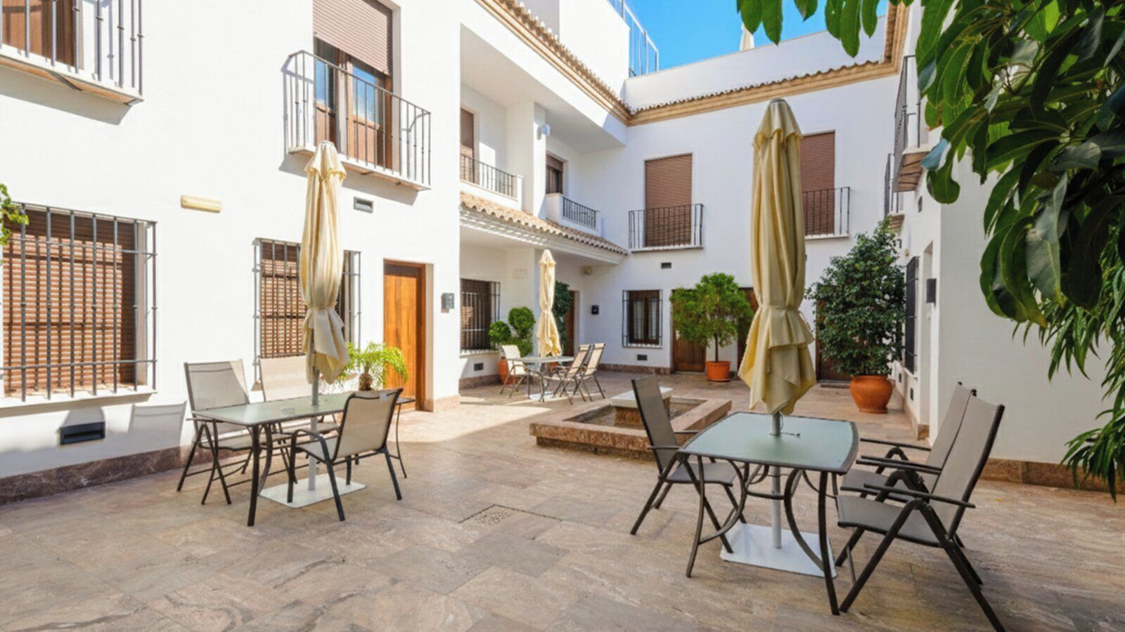 Un patio con mobiliario exterior, plantas en macetas y suelo de baldosas.