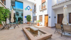 Ein Innenhof mit Außenbestuhlung, einer Wasseranlage, Topfpflanzen und einem modernen Gebäude mit Balkonen.