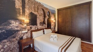 A hotel room with a large bed, two bedside lamps, a wooden nightstand, a dark wooden wardrobe, and a mural of a rocky landscape on the wall. - Ardales 5 pax by Ruralidays (Málaga)