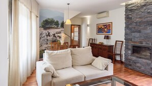 A living room with a beige sofa, a stone fireplace, and a mural of a landscape. - Ardales 5 pax by Ruralidays (Málaga)