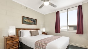 A hotel room with a large bed, wooden nightstands, a ceiling fan, a window with curtains, and a framed picture on the wall. - Regent Park (Sandy Bay)