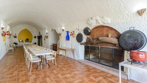 Ein Essbereich mit einem langen Tisch und Stühlen, einem Kamin mit Kochtöpfen und einer rustikalen Steinwand.