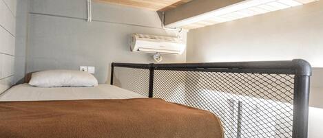 A bedroom with a bed, a headboard with a mesh design, an air conditioning unit on the wall, and a wooden ceiling.