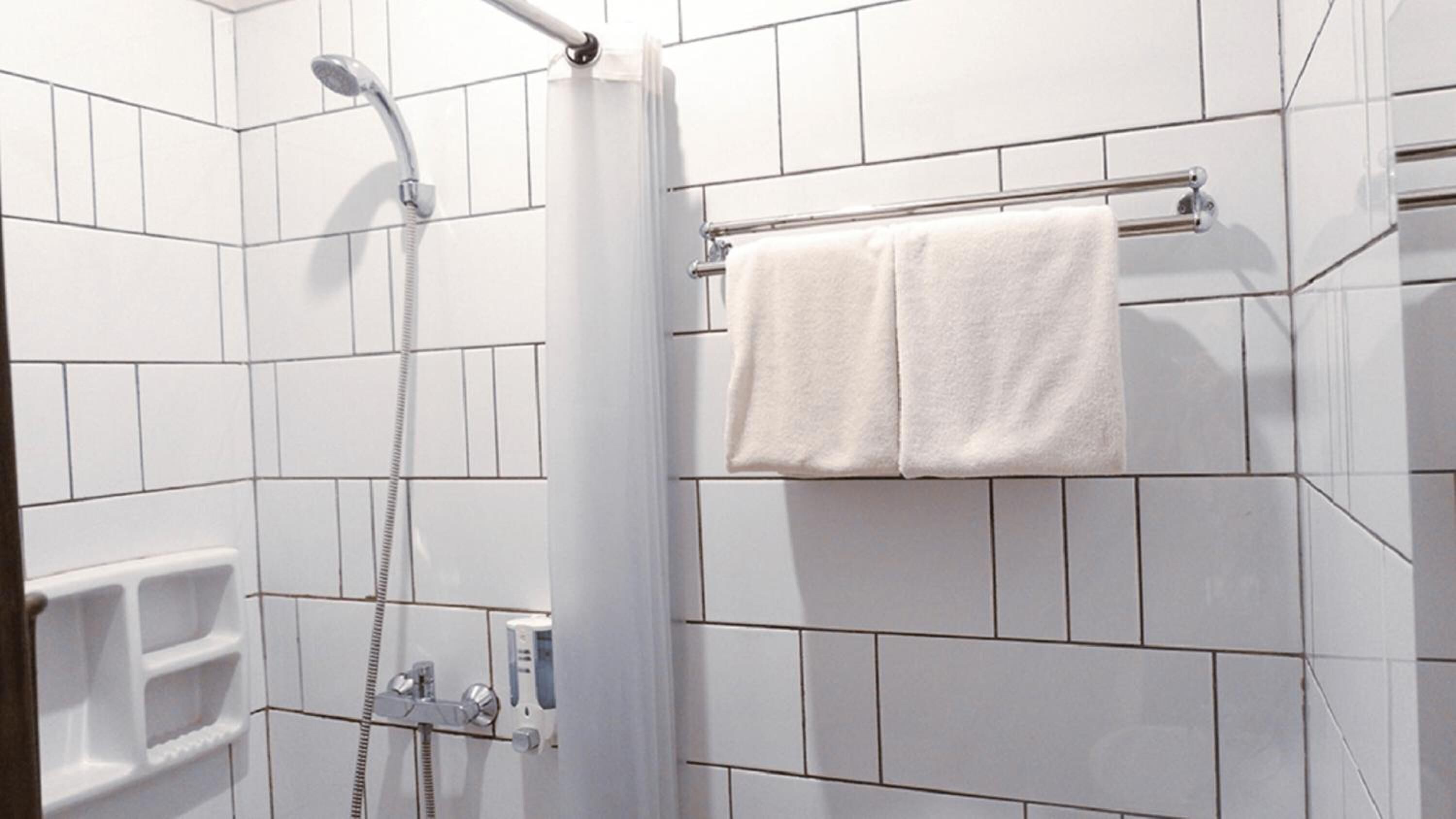A shower with a handheld showerhead and a wall-mounted faucet. There is a towel rack with two white towels.