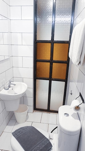Um banheiro pequeno com azulejos brancos, pia branca, vaso sanitário e box de chuveiro com painel de vidro fosco.