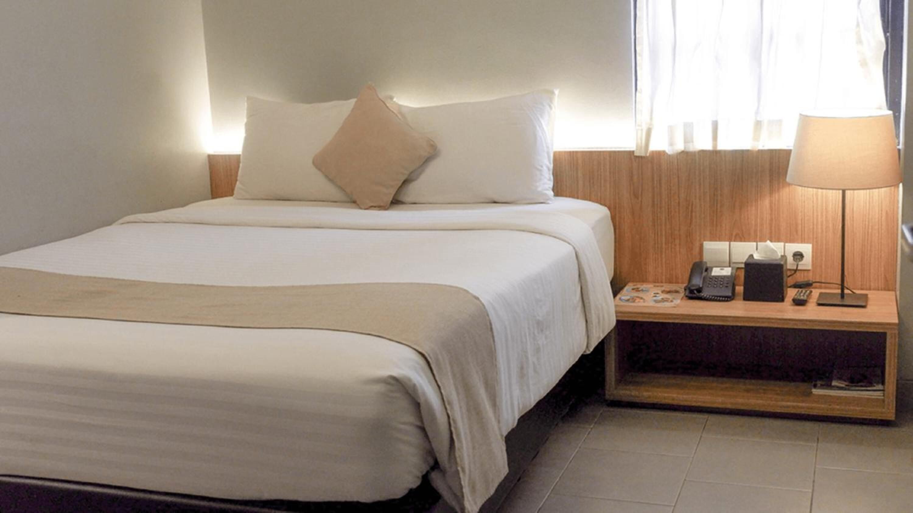 A hotel room with a bed, a bedside table with a lamp, a phone, and a small table with a tissue box.