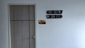 Una habitación con puerta de madera, pared blanca y dos letreros direccionales que indican los números de habitación 201 al 207 y 208 al 213.