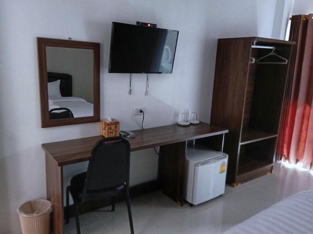 Ein Hotelzimmer mit Holzschreibtisch, Wandfernseher, kleinem Kühlschrank, Kleiderschrank und Spiegel.