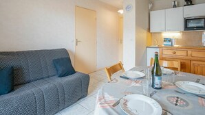 Un espacio habitable compacto con sofá, mesa de comedor para dos, zona de cocina con microondas y un reloj en la pared.