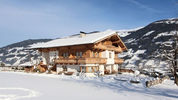 A wooden chalet with a balcony, surrounded by snow-covered mountains.