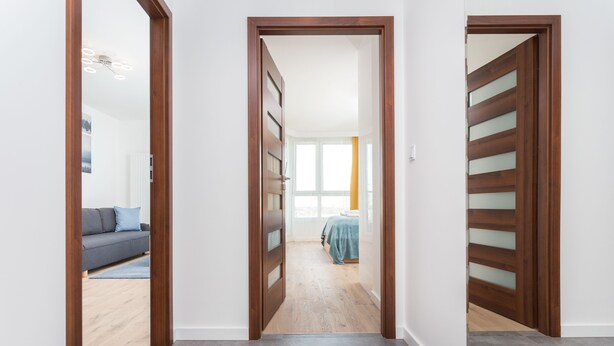 A hallway with wooden doors leading to a bedroom with a bed and a window. - Apartamenty InPoint Mogilska Tower (Kraków)