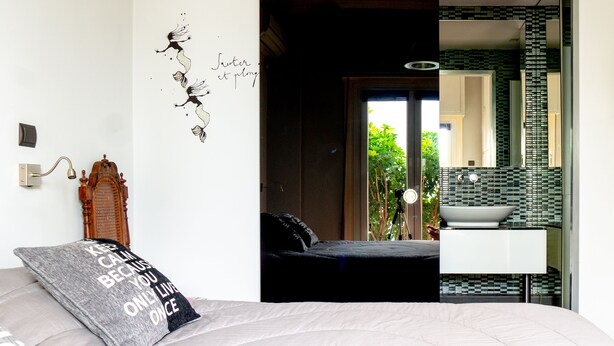 A bedroom with a bed, a nightstand, a wall with a decorative mural, and a view of the bathroom through an open door. - The Burton Luxury 1BR in Plaka, Athens (Athina)