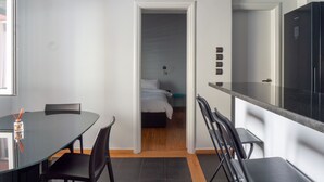 A modern kitchen with a black countertop and a dining area with a glass table and black chairs. - The Burton Luxury 1BR in Plaka, Athens (Athina)
