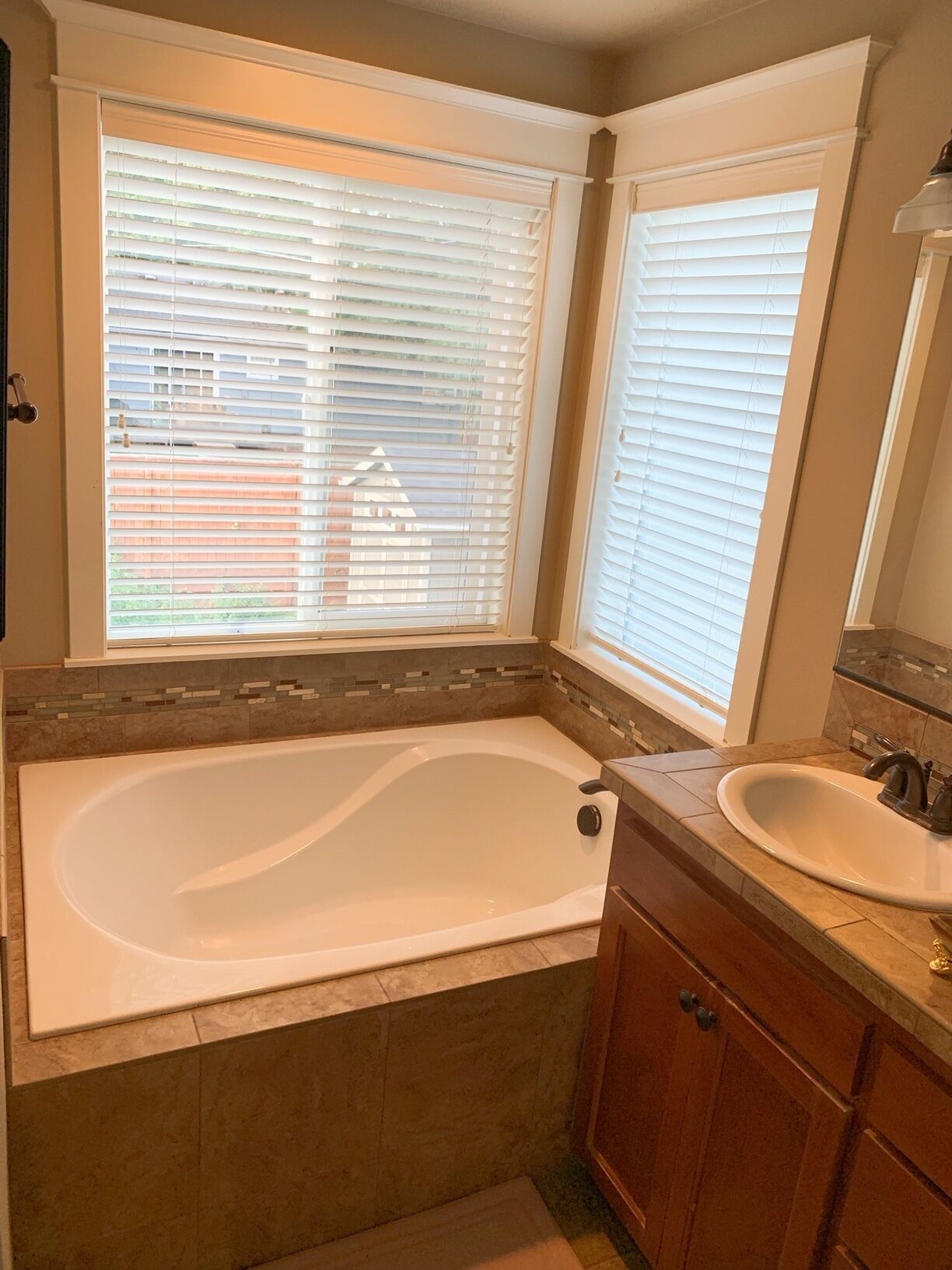 A bathroom with a large bathtub, a sink, and a window with blinds.