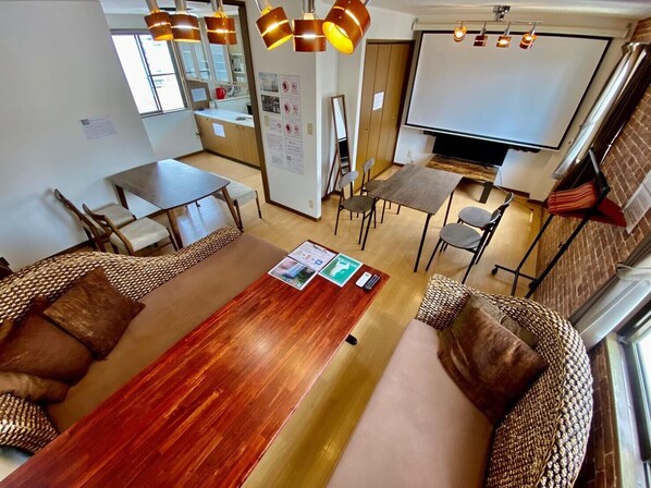 A modern hotel room with a wooden dining table, two sofas, a TV, and a kitchenette.