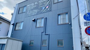 Un bâtiment avec une enseigne indiquant « HÔTEL EL TOCHIGI3 », doté de nombreuses fenêtres et d’une façade bleue.