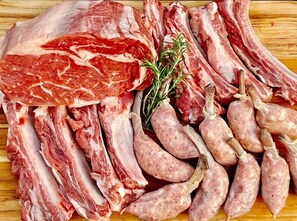 A variety of raw meats including ribs and sausages on a wooden surface.