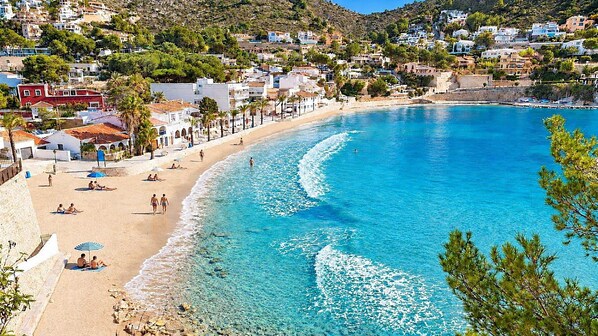 A coastal town with a beach, clear blue waters, and buildings with balconies.