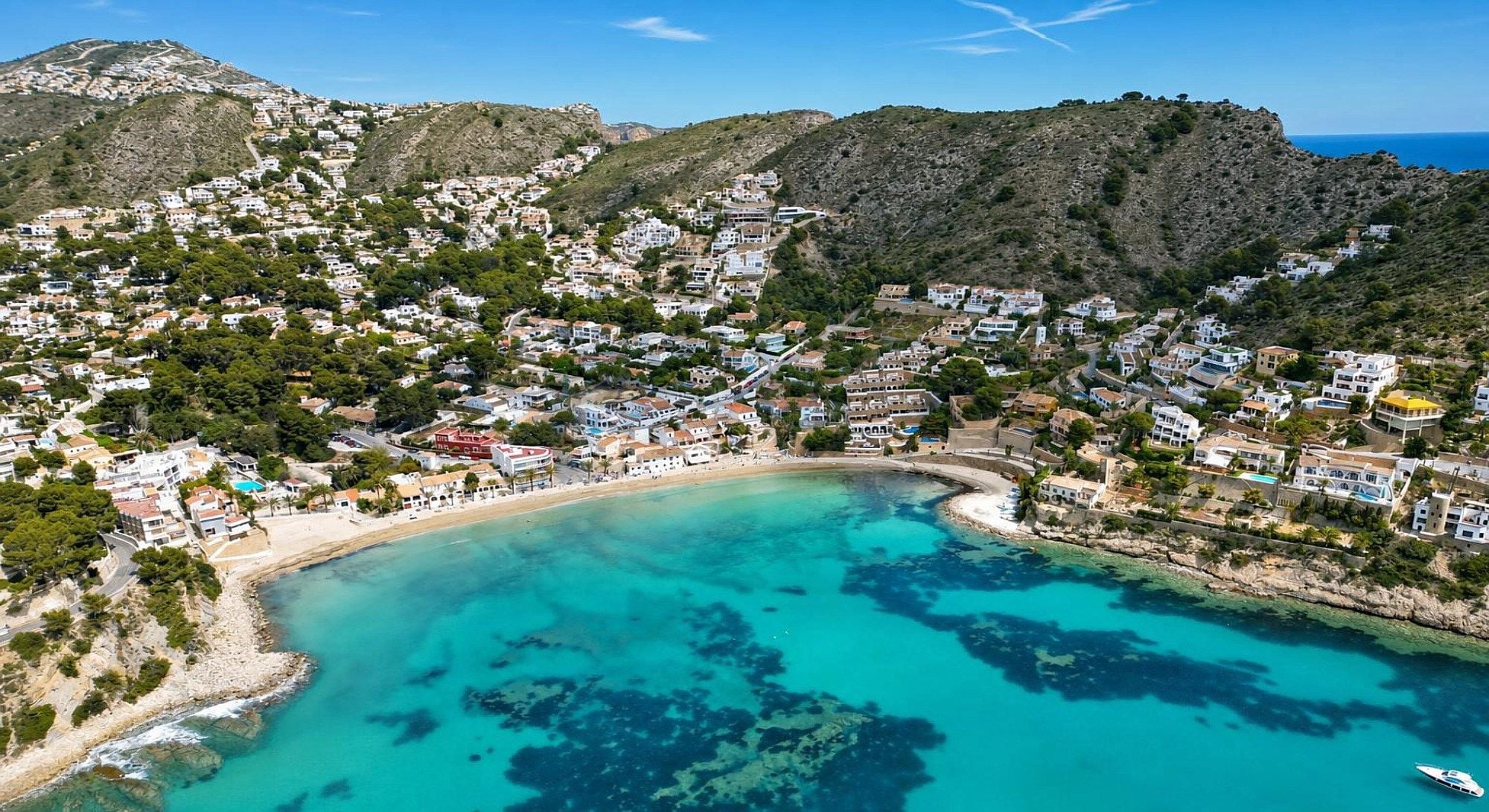 A coastal town with a beach, houses, and a mountainous backdrop.