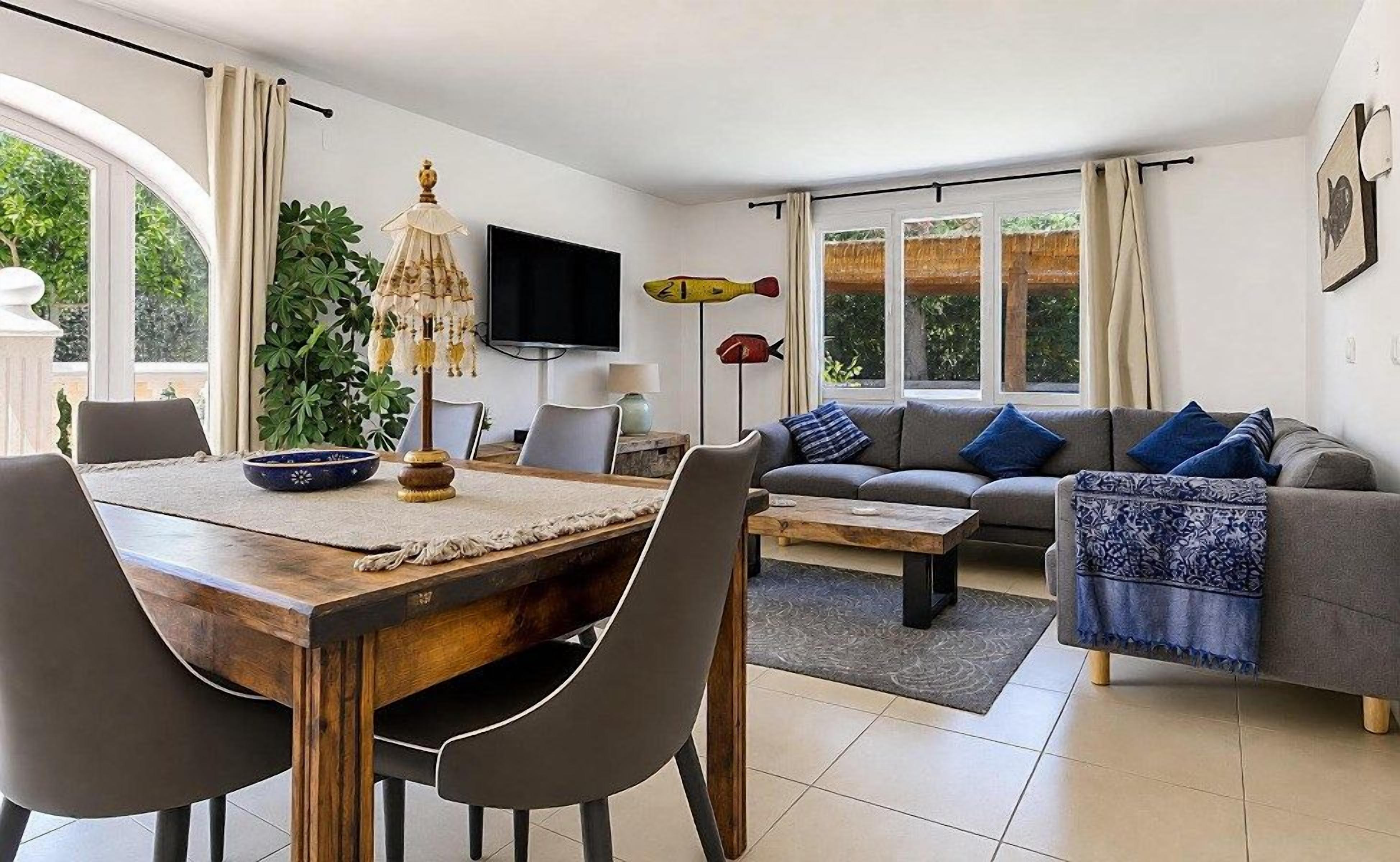 Una sala de estar moderna con un sofá, una mesa de comedor, sillas, un televisor y un ventanal grande.